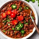 Overhead view of slow cooker pinto beans in a bowl, topped with sliced cherry tomatoes and jalapeños.