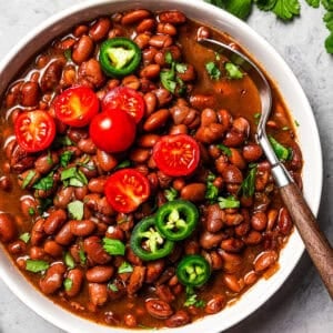 Overhead view of slow cooker pinto beans in a bowl, topped with sliced cherry tomatoes and jalapeños.