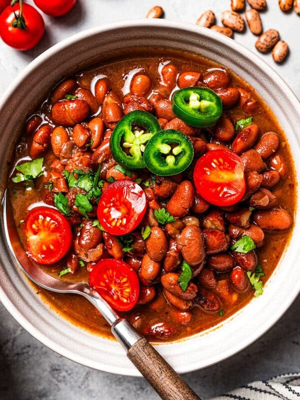 A bowl of pinto beans garnished with cherry tomatoes and jalapeños.