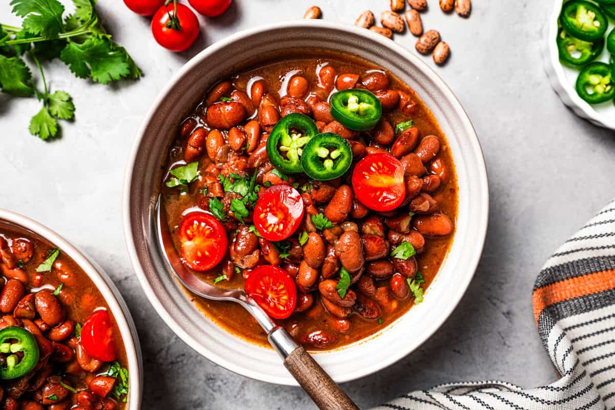 Slow cooker pinto beans are full of flavor and so easy to make. Add dry beans to the crock pot in the morning, and they’re tender by dinner! A bowl of pinto beans garnished with cherry tomatoes and jalapeños.