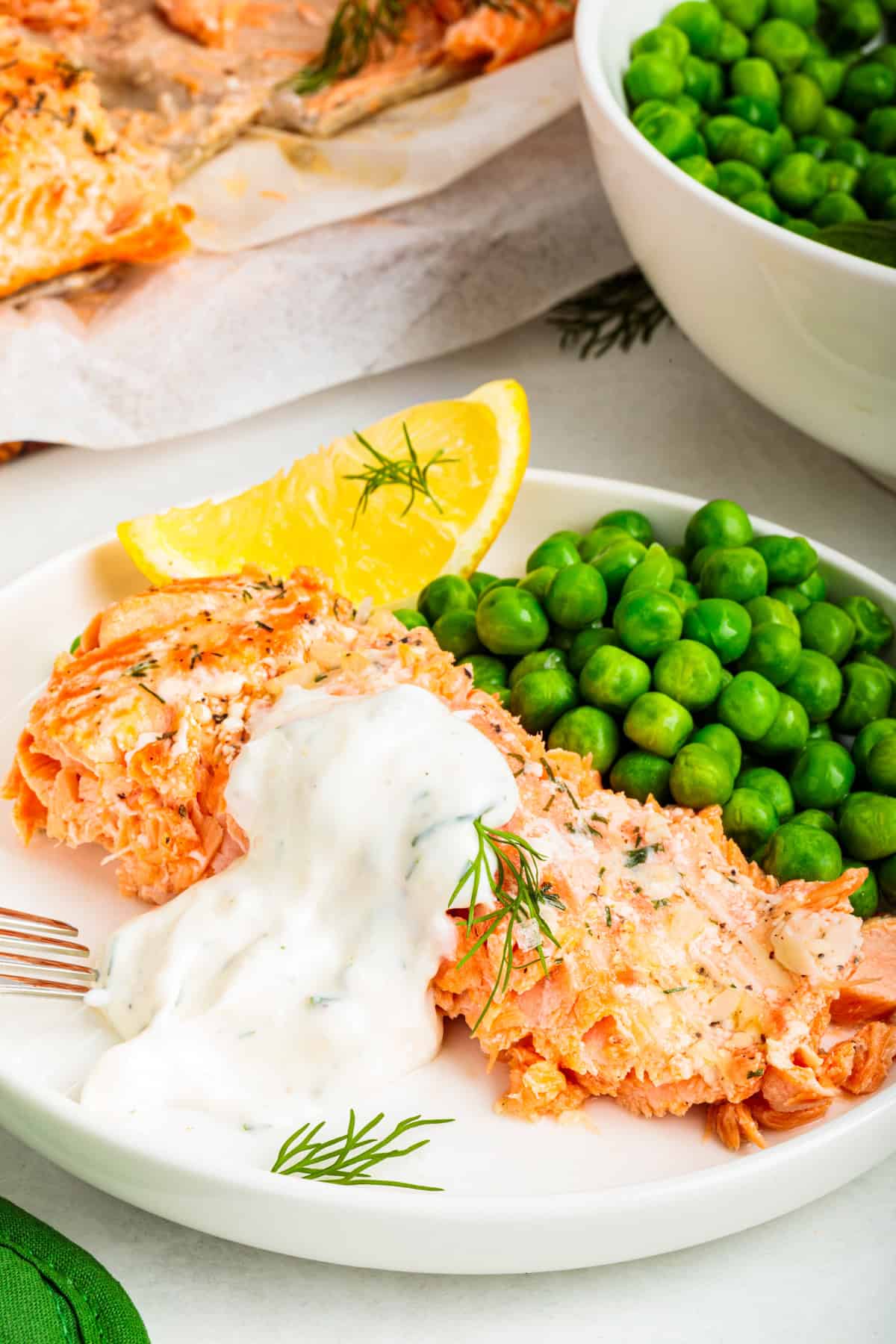Baked steelhead trout with lemon, butter, garlic, and fresh dill. This easy steelhead trout recipe is tender, flaky, and ready in 30 minutes. A serving of steelhead trout on a plate with a side of peas and a dollop of creamy horseradish dill sauce on top of the fish.