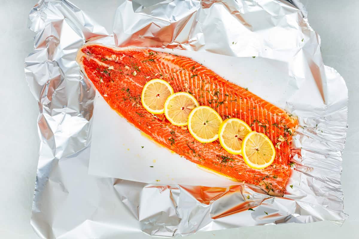Baked steelhead trout with lemon, butter, garlic, and fresh dill. This easy steelhead trout recipe is tender, flaky, and ready in 30 minutes. A whole raw steelhead trout fillet on a large piece of foil, topped with slices of lemon.