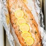 A whole baked trout fillet on a large piece of foil, topped with slices of lemon.