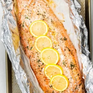 A whole baked trout fillet on a large piece of foil, topped with slices of lemon.