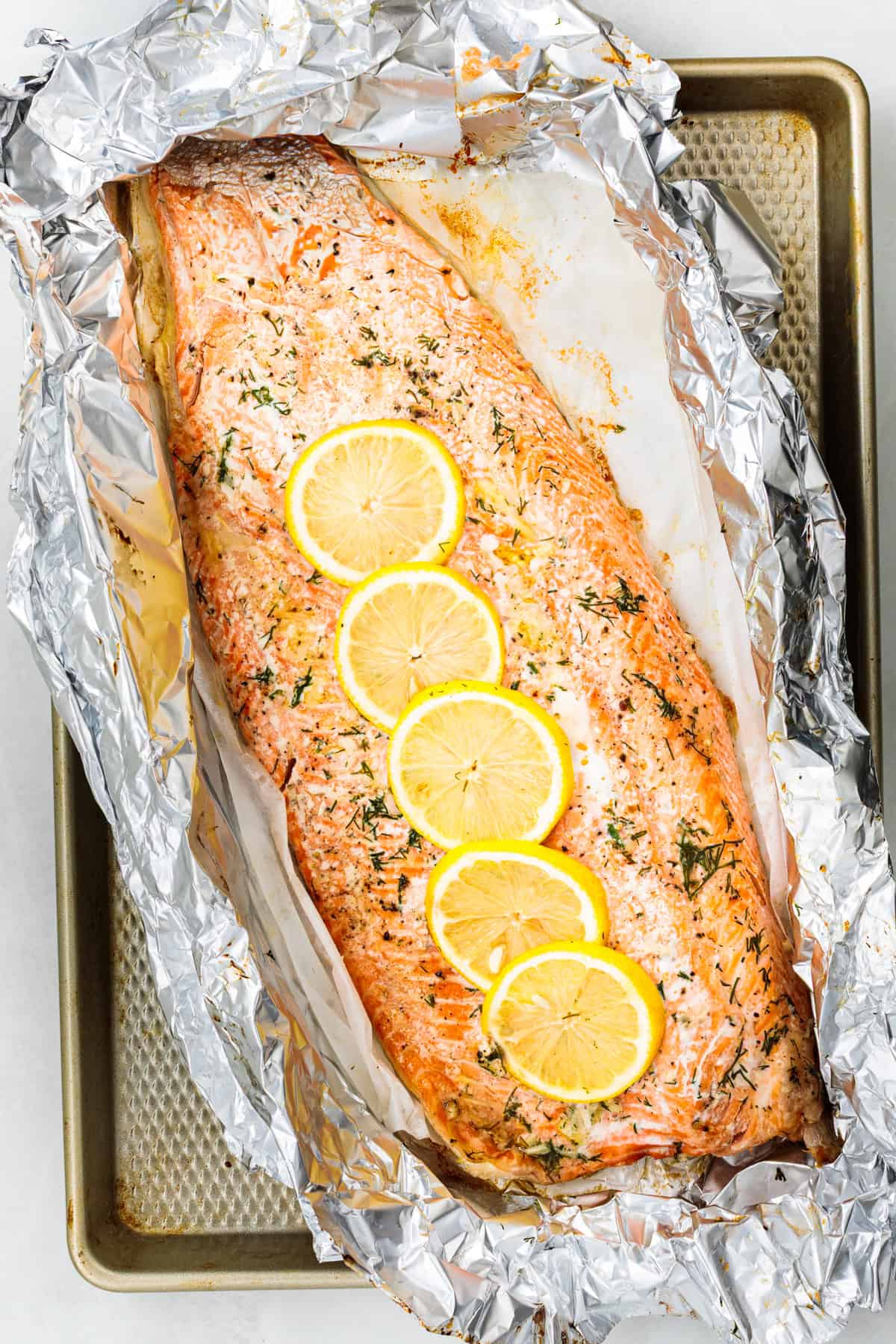 Baked steelhead trout with lemon, butter, garlic, and fresh dill. This easy steelhead trout recipe is tender, flaky, and ready in 30 minutes. A whole baked trout fillet on a large piece of foil, topped with slices of lemon.