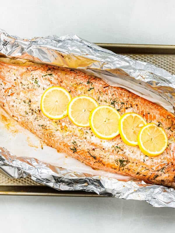 A whole baked trout fillet on a large piece of foil, topped with slices of lemon.