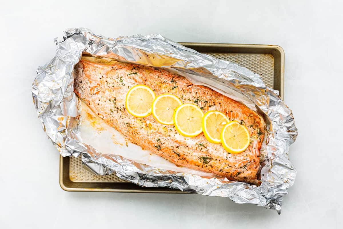 Baked steelhead trout with lemon, butter, garlic, and fresh dill. This easy steelhead trout recipe is tender, flaky, and ready in 30 minutes. A whole baked trout fillet on a large piece of foil, topped with slices of lemon.