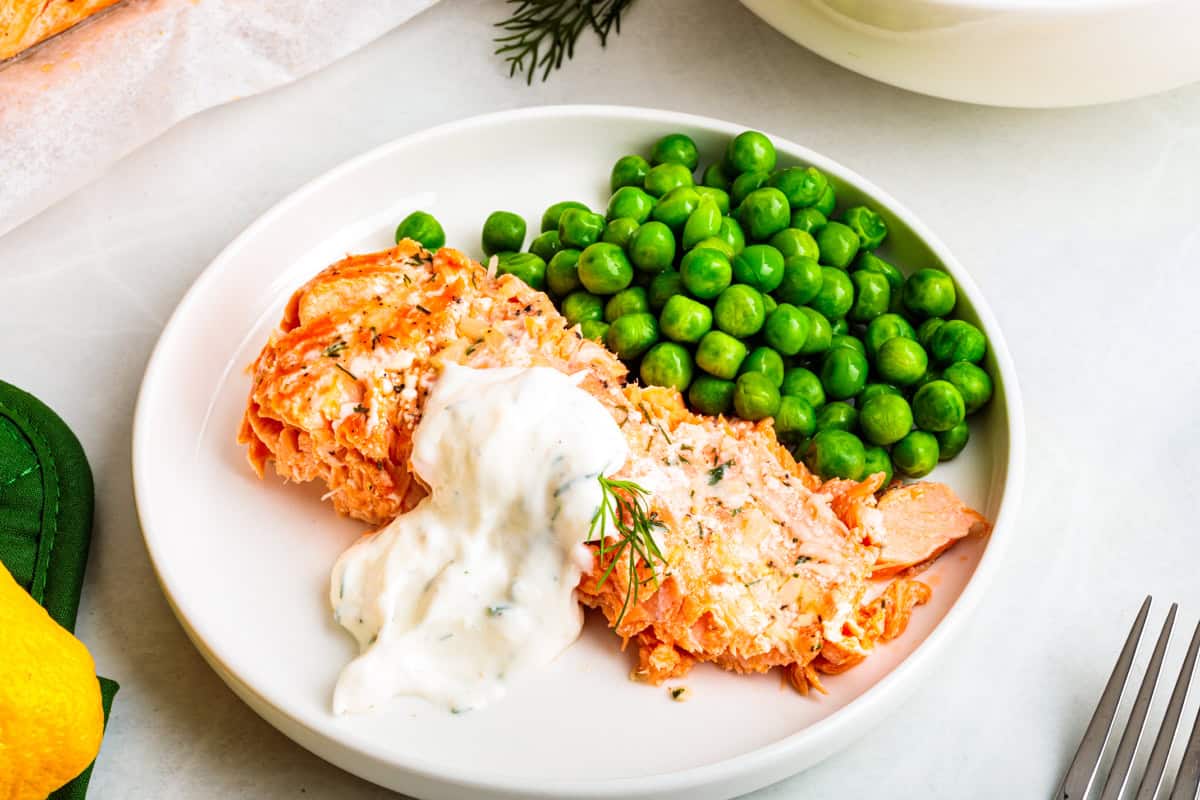 Baked steelhead trout with lemon, butter, garlic, and fresh dill. This easy steelhead trout recipe is tender, flaky, and ready in 30 minutes. A serving of steelhead trout on a plate with a side of peas and a dollop of creamy horseradish dill sauce on top of the fish.