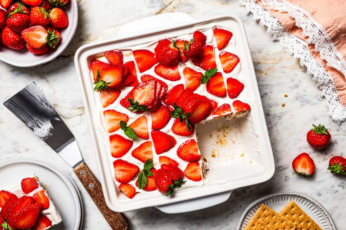 This no-bake strawberry icebox cake is an easy overnight dessert with layers of graham crackers, fresh strawberries, and fluffy whipped cream. Strawberry icebox cake in a ceramic dish with a corner slice missing.