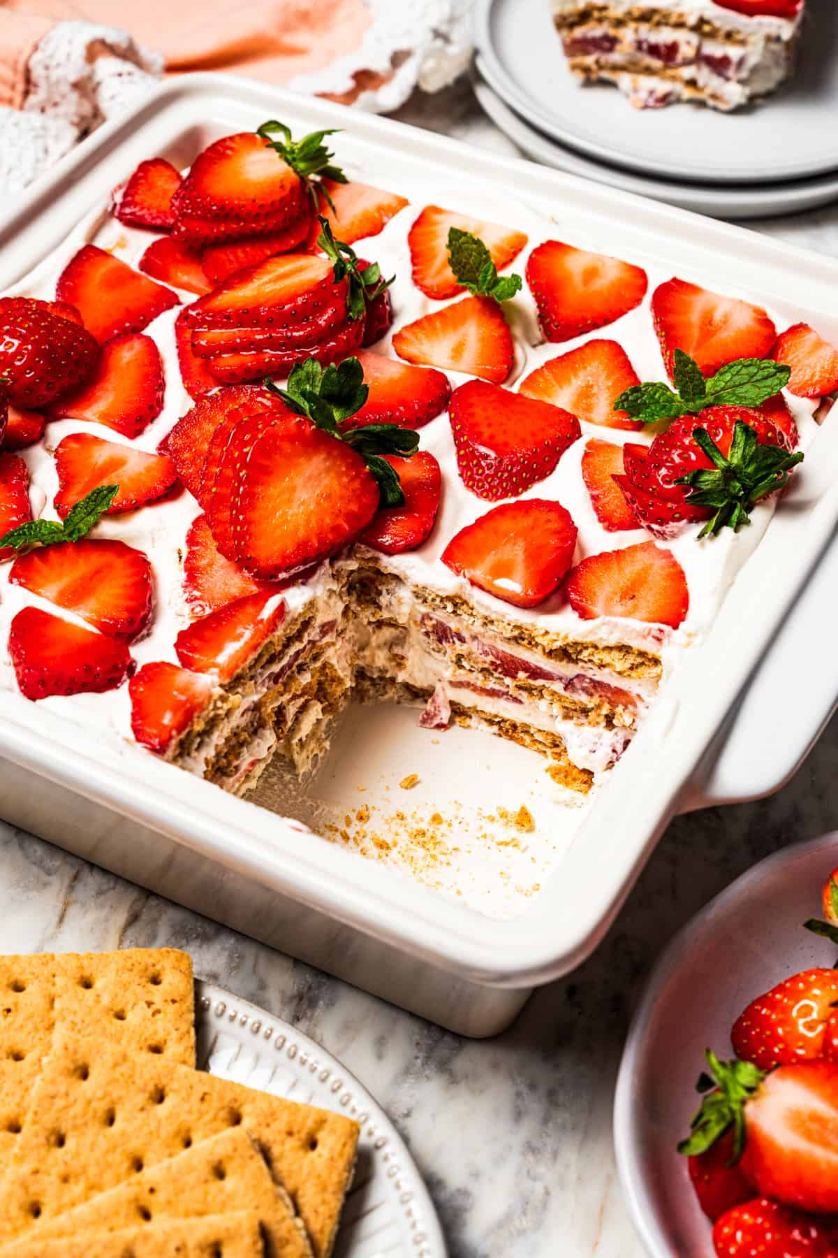 This no-bake strawberry icebox cake is an easy overnight dessert with layers of graham crackers, fresh strawberries, and fluffy whipped cream. Strawberry icebox cake in a ceramic dish with a slice missing from the corner.