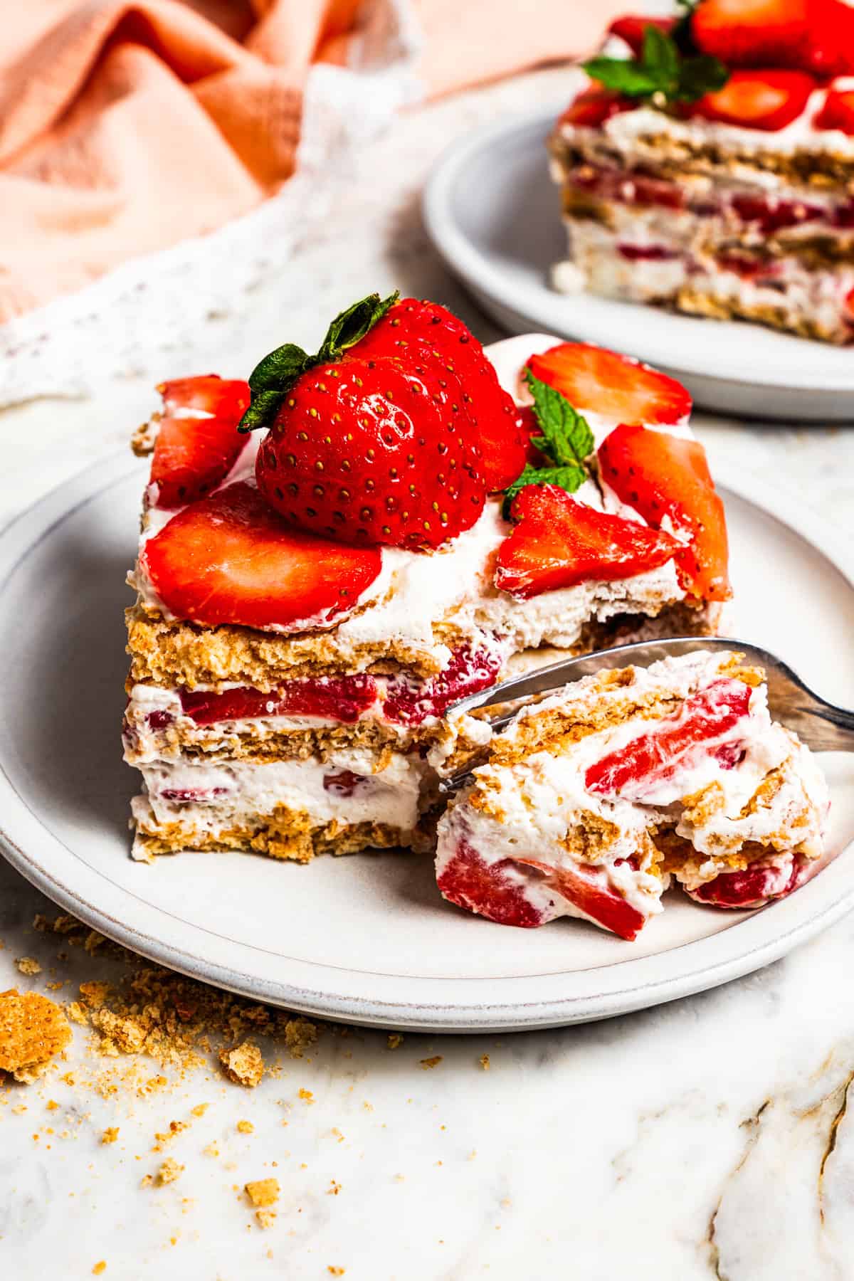 This no-bake strawberry icebox cake is an easy overnight dessert with layers of graham crackers, fresh strawberries, and fluffy whipped cream. A fork cutting into a slice of icebox cake.