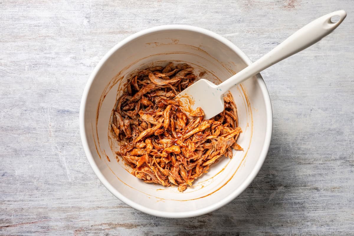 These BBQ pulled pork sliders are sweet, smoky, savory, and easy to make with leftover pulled pork, melted cheese, and fluffy Hawaiian rolls. Pulled pork mixed with barbecue sauce in a bowl.