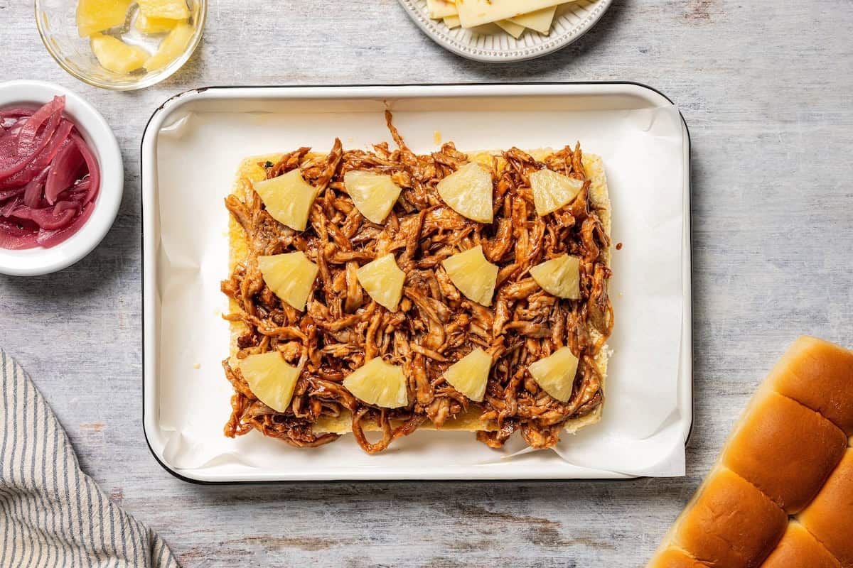 These BBQ pulled pork sliders are sweet, smoky, savory, and easy to make with leftover pulled pork, melted cheese, and fluffy Hawaiian rolls. Pineapple chunks placed on top of BBQ pulled pork on Hawaiian rolls.