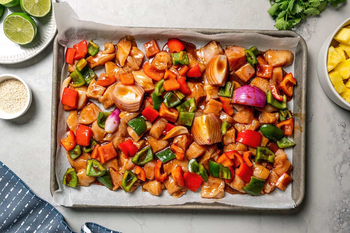 Marinated chicken cubes combined with bell peppers and pineapple on a baking sheet.