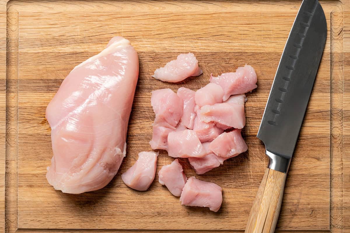 Creamy slow cooker chicken and rice is an easy one-pot dinner with rice, condensed mushroom soup, melty cheddar, onions, and juicy chicken. Chicken breast chopped into small pieces on a wooden cutting board.