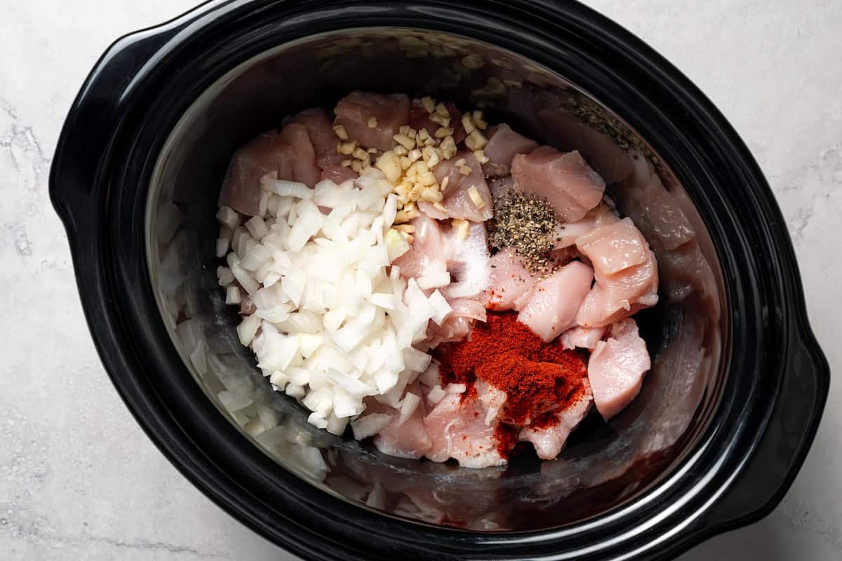 Creamy slow cooker chicken and rice is an easy one-pot dinner with rice, condensed mushroom soup, melty cheddar, onions, and juicy chicken. Onions, garlic, and seasonings added to chicken in the slow cooker.