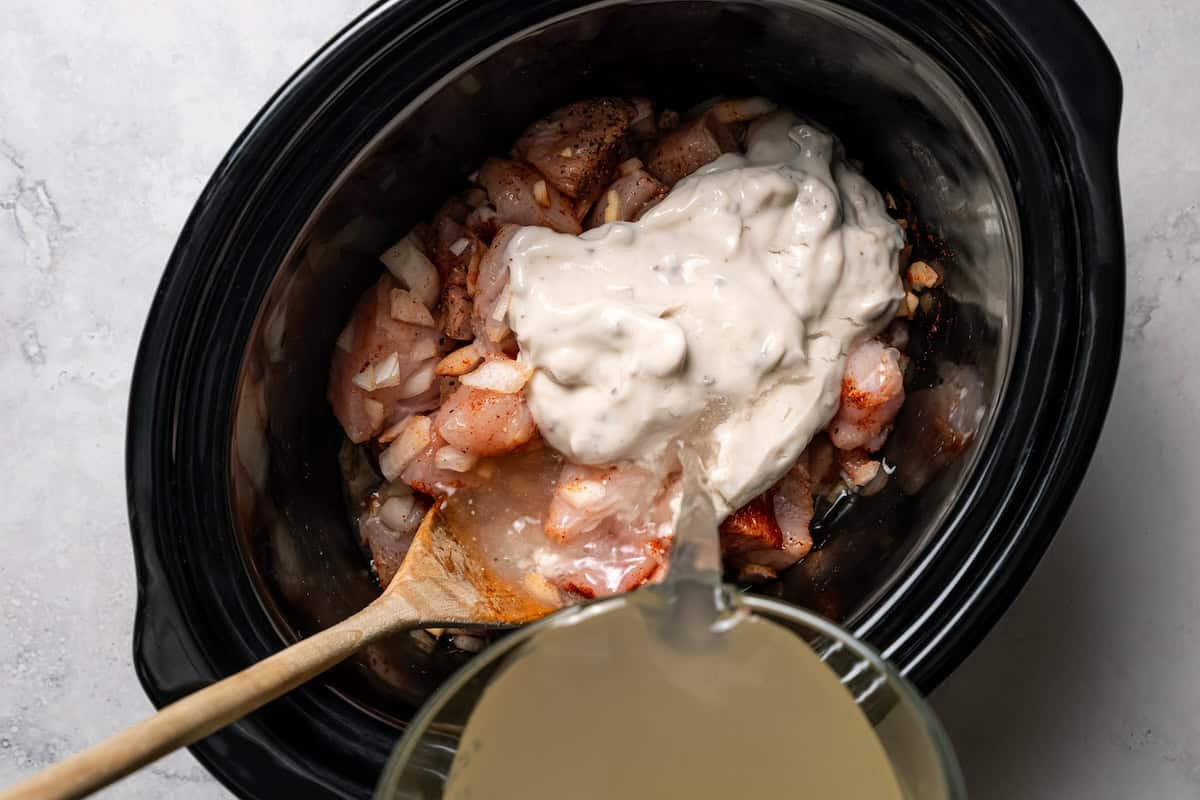 Creamy slow cooker chicken and rice is an easy one-pot dinner with rice, condensed mushroom soup, melty cheddar, onions, and juicy chicken. Adding broth and canned cream of mushroom soup to chicken in the slow cooker.