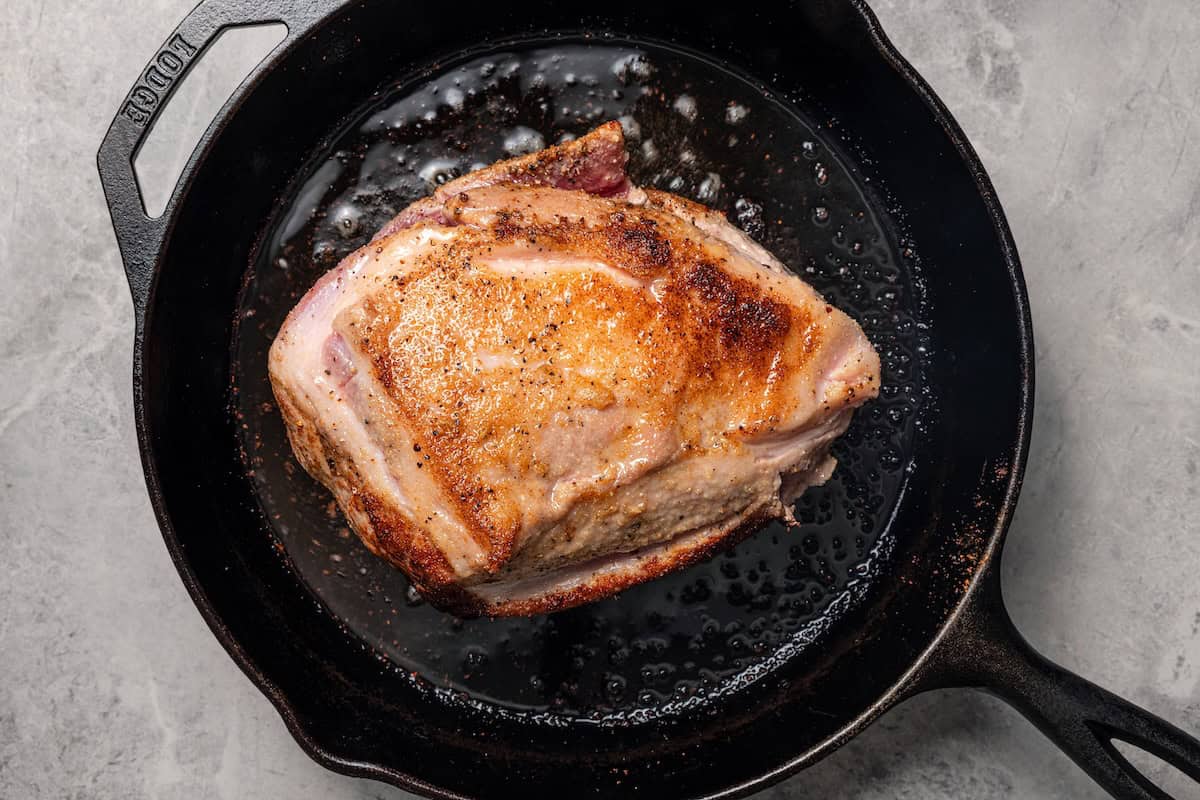 This tender, juicy slow cooker pork shoulder needs only 10 minutes of prep! It's slowly braised with hearty veggies for a cozy one-pot meal. Seared and seasoned pork shoulder in a skillet.