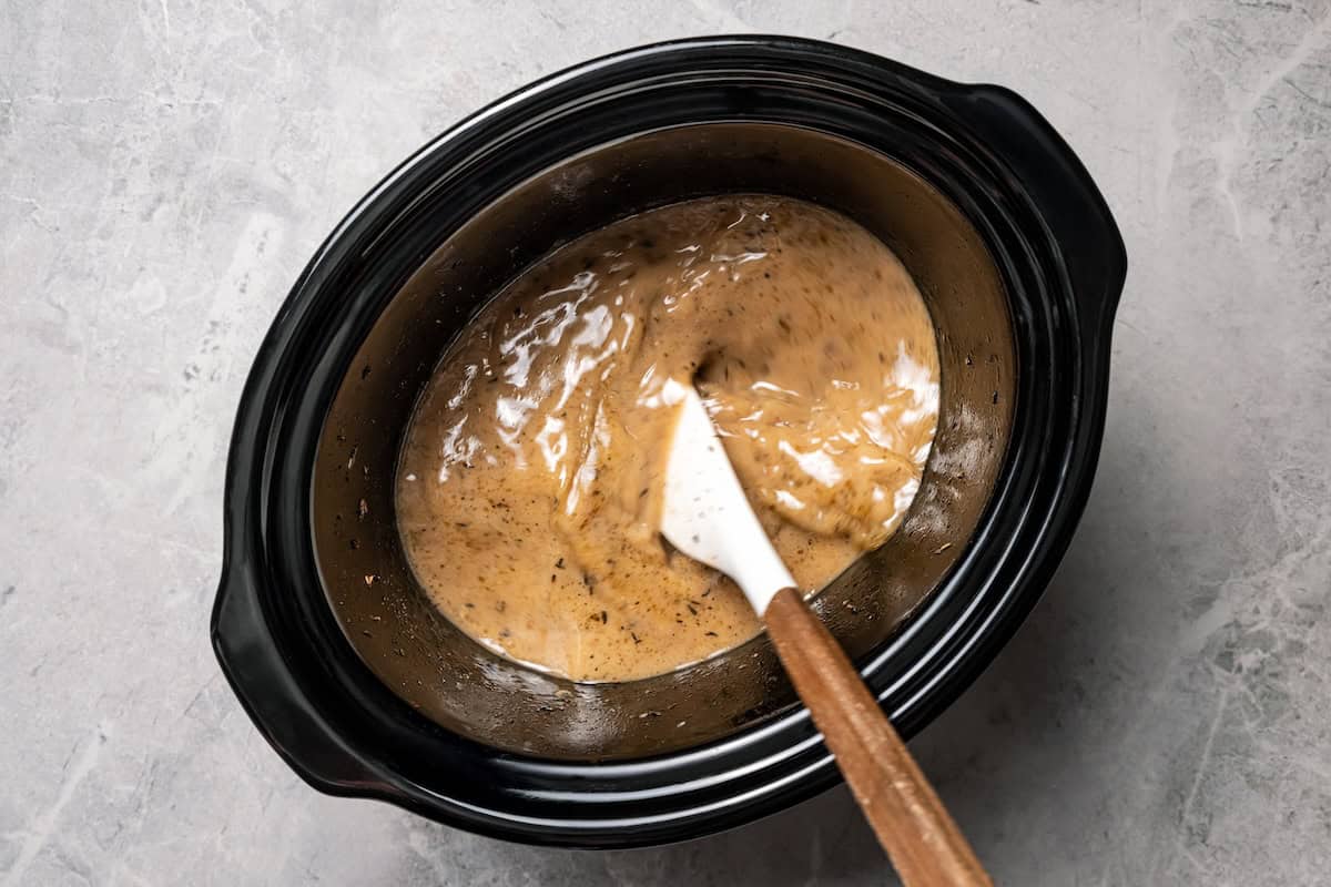 This tender, juicy slow cooker pork shoulder needs only 10 minutes of prep! It's slowly braised with hearty veggies for a cozy one-pot meal. Stirring a slurry into the cooking juices to make a gravy.