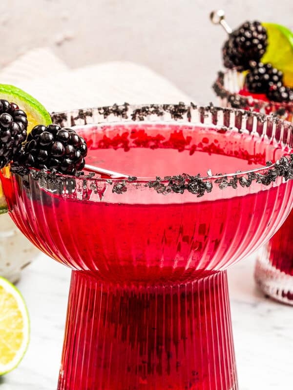 Two blackberry margaritas in salt-rimmed glasses garnished with fresh berries and lime slices.