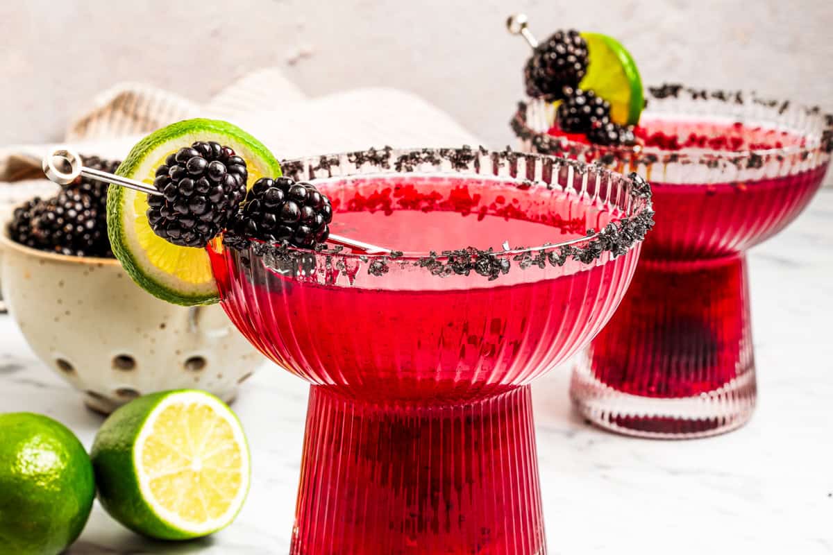 A blackberry margarita puts a refreshing, sweet-tart spin on the classic cocktail, with fresh muddled blackberries, tequila blanco, and lime. Two blackberry margaritas in salt-rimmed glasses garnished with fresh berries and lime slices.