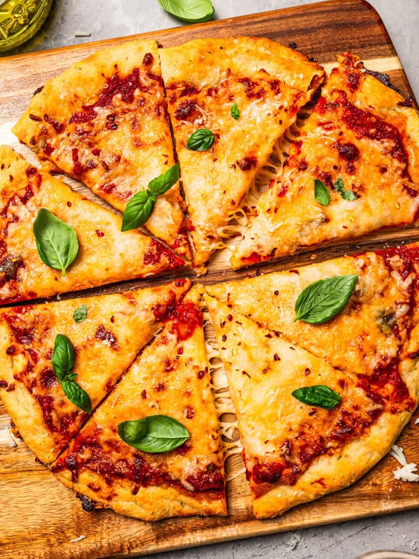 Cottage cheese pizza crust topped with margherita toppings, cut into slices on a wooden cutting board.
