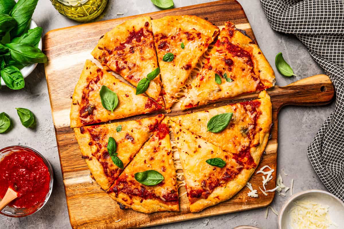 Cottage cheese pizza crust topped with margherita toppings, cut into slices on a wooden cutting board.
