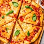 A hand lifting a slice of high-protein cottage cheese pizza from a wooden cutting board.