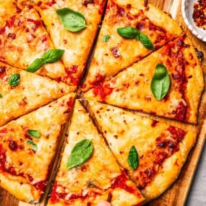 A hand lifting a slice of high-protein cottage cheese pizza from a wooden cutting board.