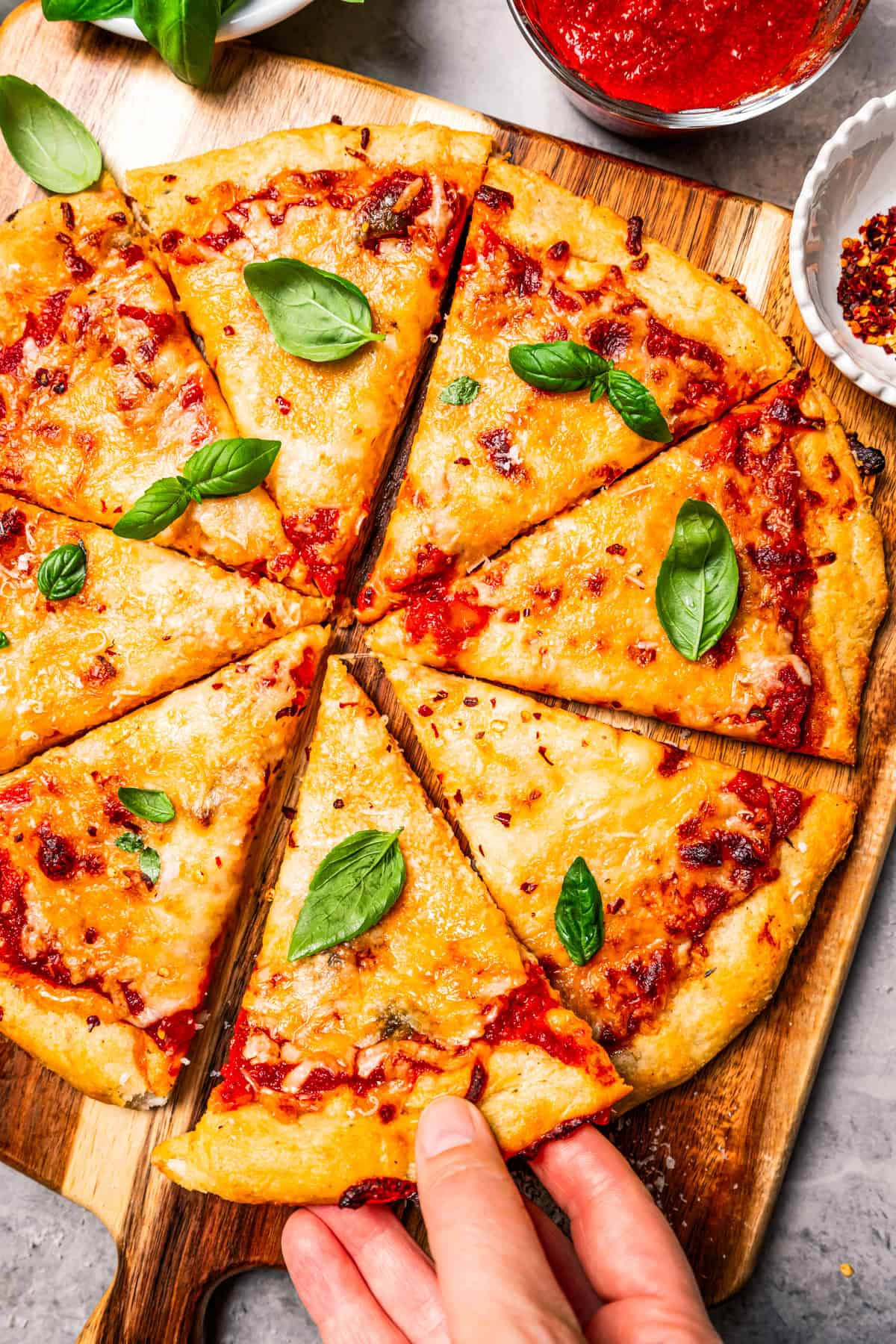 A hand lifting a slice of high-protein cottage cheese pizza from a wooden cutting board.