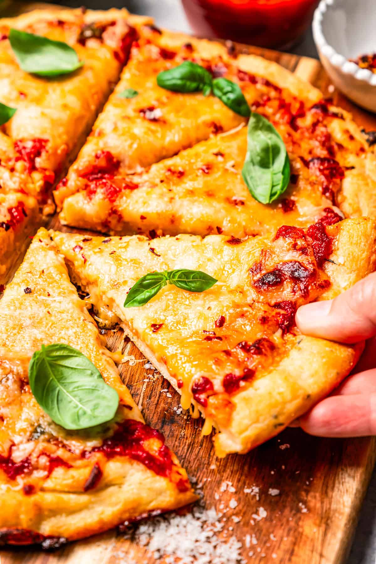 A hand lifting a slice of cottage cheese pizza from a wooden cutting board.