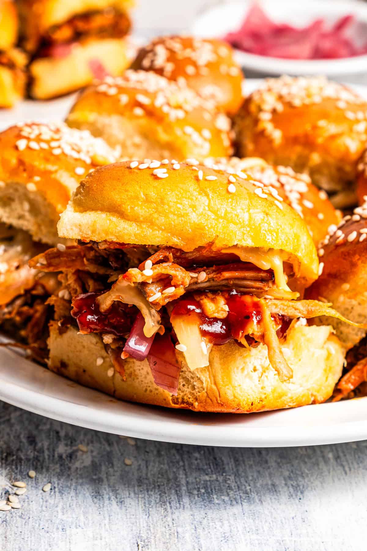 These BBQ pulled pork sliders are sweet, smoky, savory, and easy to make with leftover pulled pork, melted cheese, and fluffy Hawaiian rolls. Close-up of a pulled pork slider served on a platter with more sliders.