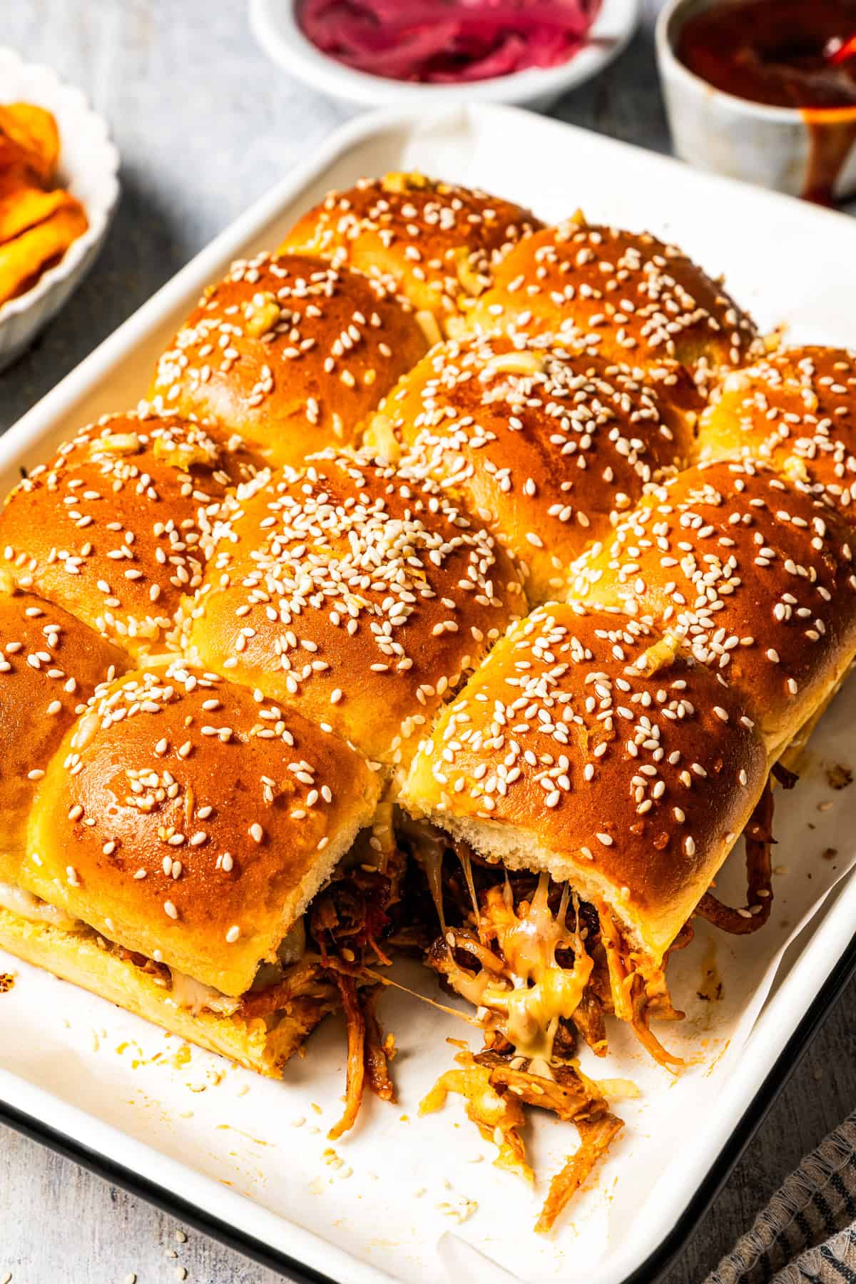 These BBQ pulled pork sliders are sweet, smoky, savory, and easy to make with leftover pulled pork, melted cheese, and fluffy Hawaiian rolls. Baked pulled pork sliders on a baking pan with a slider missing from the corner.