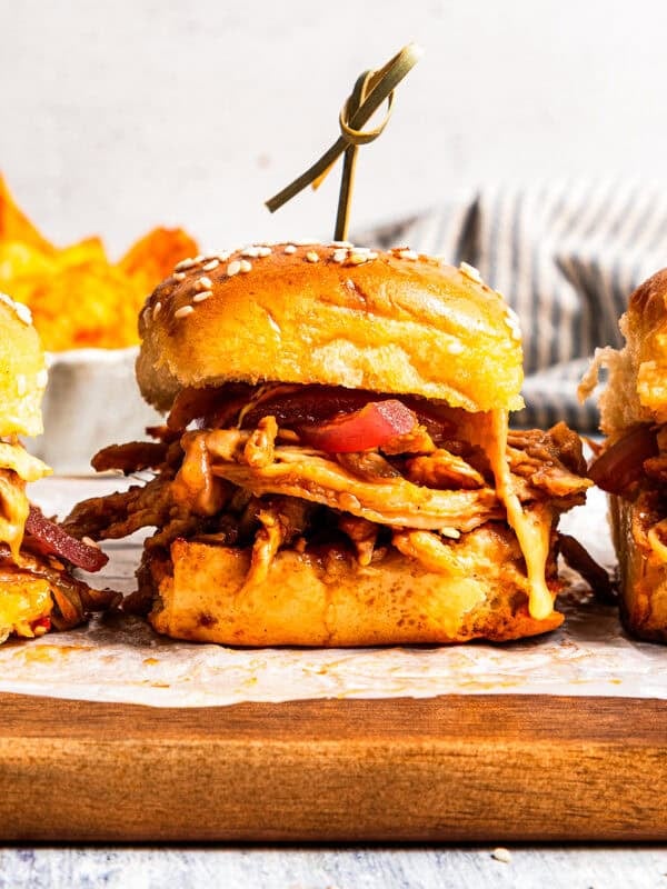 Three pulled pork sliders on a parchment-lined wooden board.