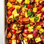 A baking sheet of chicken bites with bell peppers, red onions, and pineapple to make Hawaiian chicken.