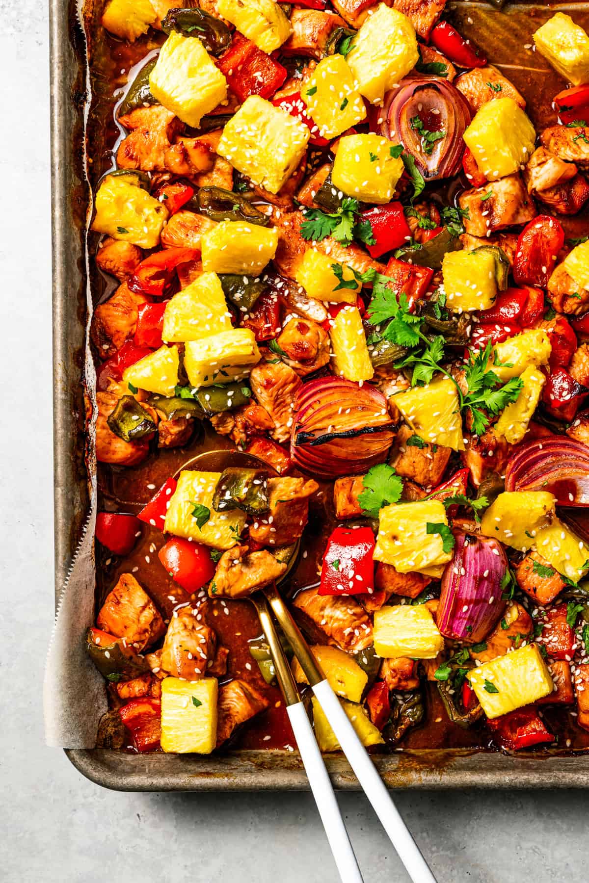 A baking sheet of chicken bites with bell peppers, red onions, and pineapple to make Hawaiian chicken.