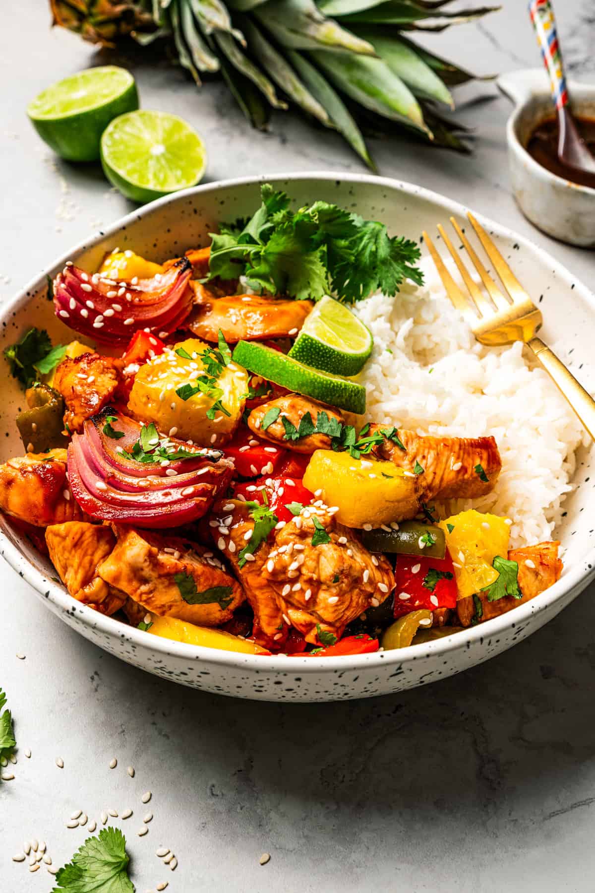 A bowl of rice topped with chicken bites, bell pepper slices, onion slices, and pineapple chunks.