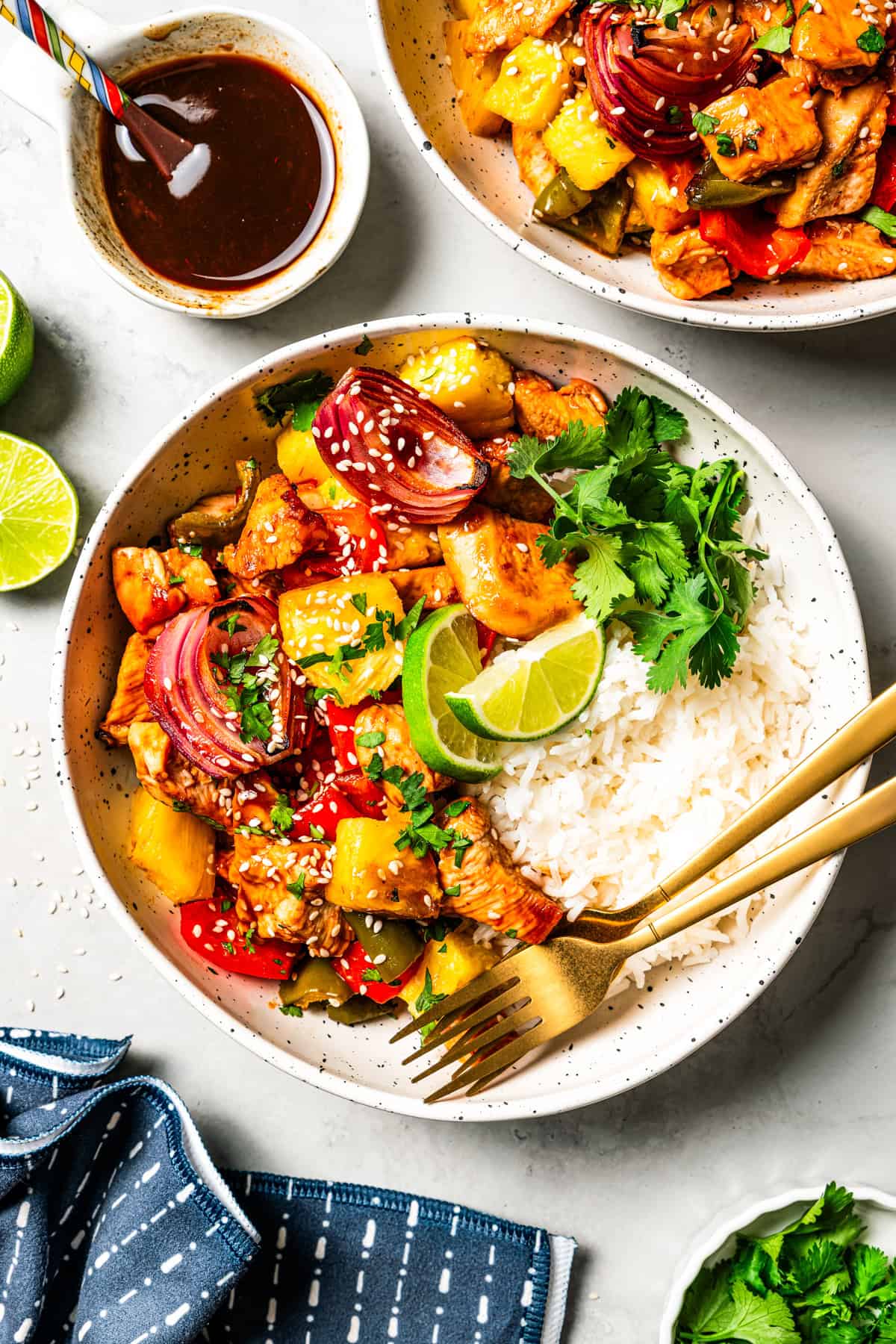 A bowl of sheet pan Hawaiian chicken featuring rice topped with chicken bites, bell pepper slices, onion slices, and pineapple chunks.