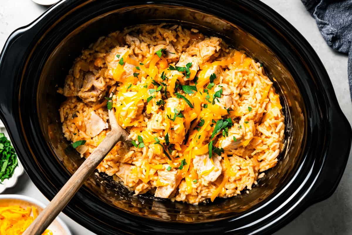 Creamy slow cooker chicken and rice is an easy one-pot dinner with rice, condensed mushroom soup, melty cheddar, onions, and juicy chicken. Overhead view of cheesy cream of mushroom chicken and rice in the slow cooker.