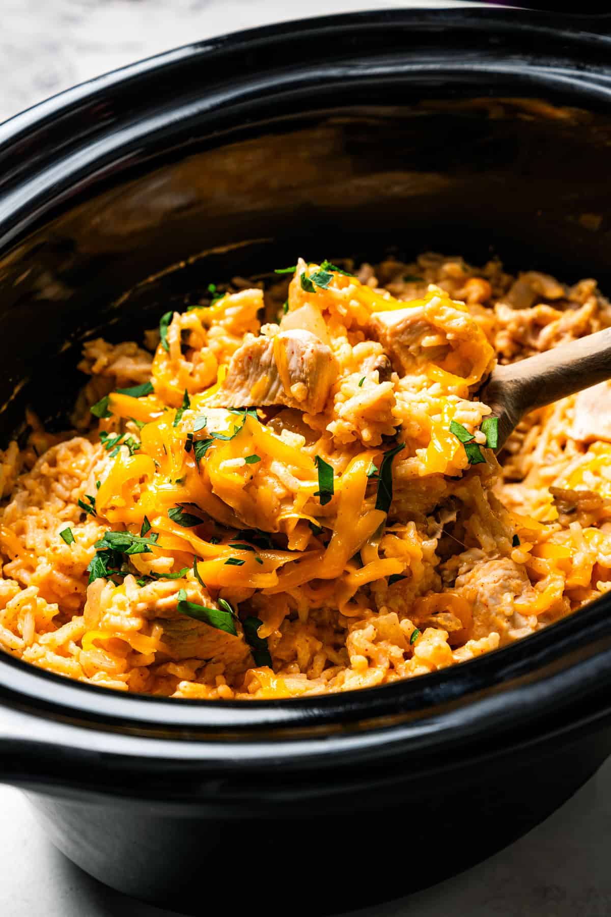 Creamy slow cooker chicken and rice is an easy one-pot dinner with rice, condensed mushroom soup, melty cheddar, onions, and juicy chicken. A spoon scooping cream of mushroom chicken and rice inside the slow cooker.
