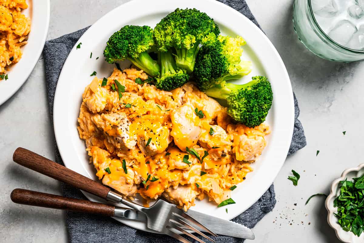 Creamy slow cooker chicken and rice is an easy one-pot dinner with rice, condensed mushroom soup, melty cheddar, onions, and juicy chicken. A serving of slow cooker cream of mushroom chicken and rice next to steamed broccoli on a plate.
