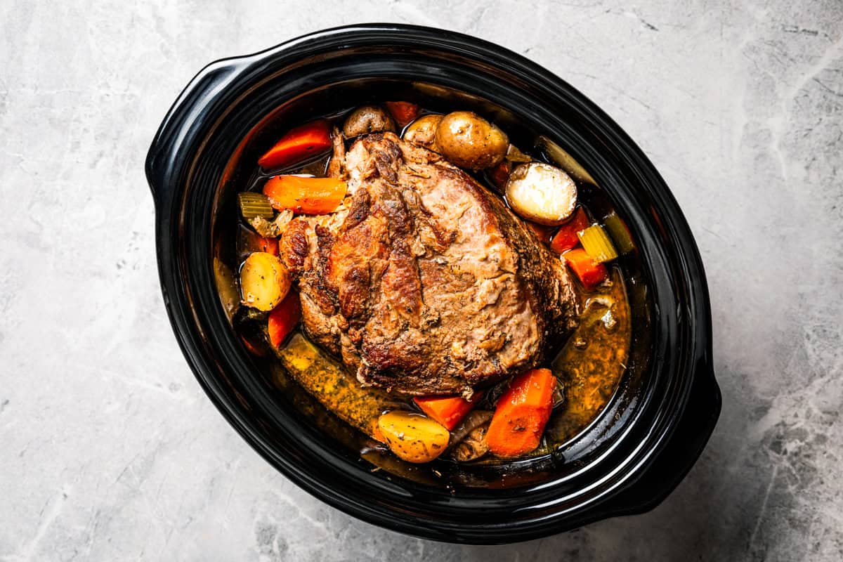 This tender, juicy slow cooker pork shoulder needs only 10 minutes of prep! It's slowly braised with hearty veggies for a cozy one-pot meal. Cooked pork shoulder with veggies inside the slow cooker.