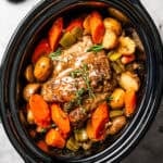 Cooked pork shoulder in the slow cooker with carrots and potatoes.