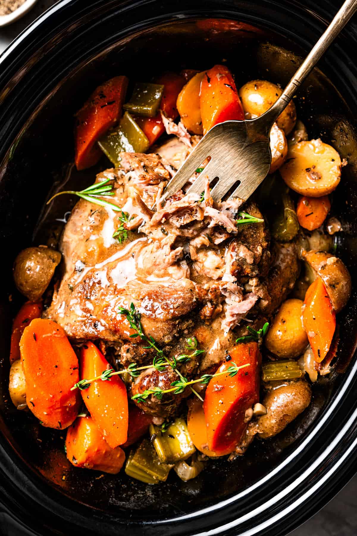 This tender, juicy slow cooker pork shoulder needs only 10 minutes of prep! It's slowly braised with hearty veggies for a cozy one-pot meal. A fork pulling apart tender pork shoulder in the slow cooker.
