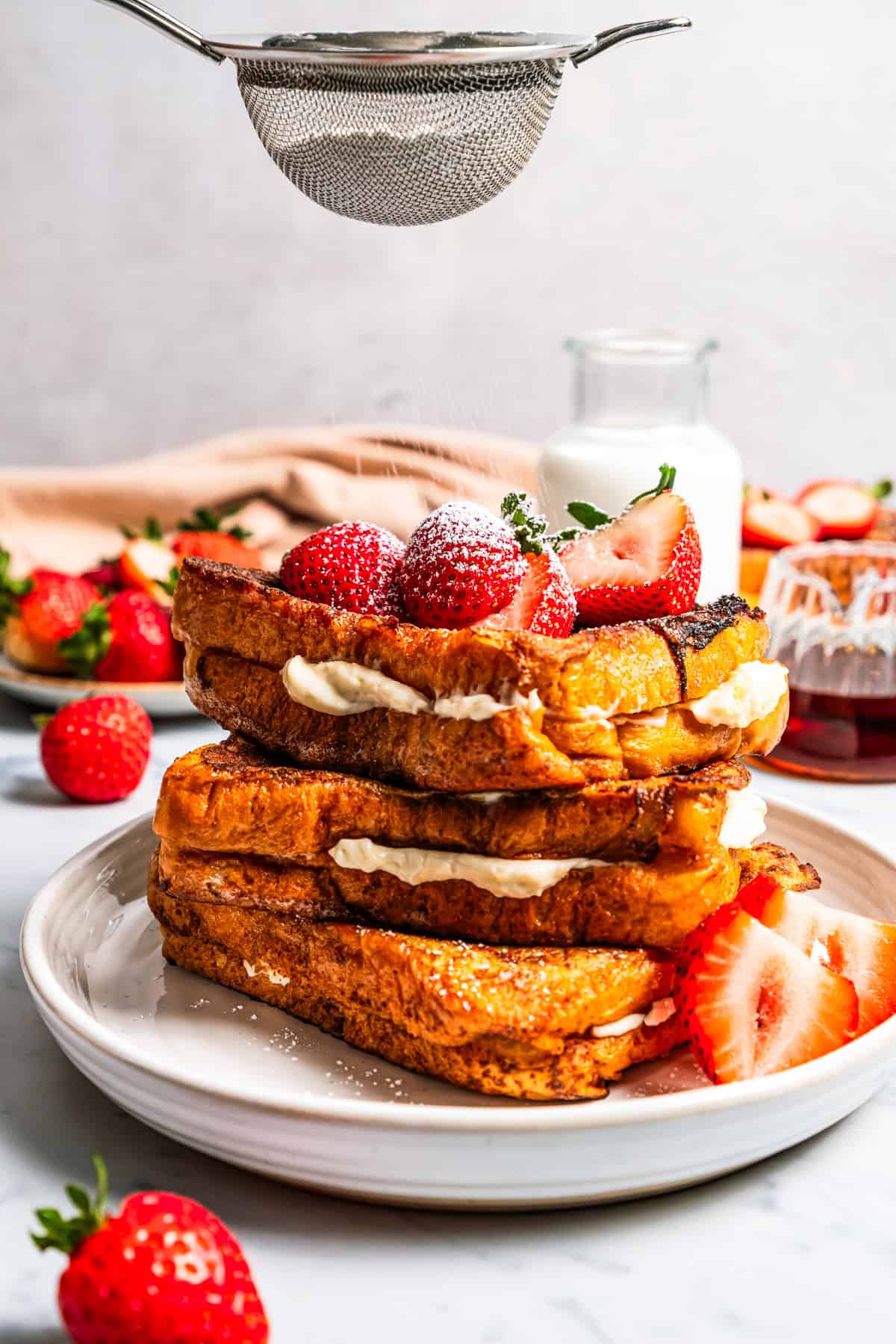 Make this cream cheese stuffed French toast with thick slices of custard-dipped brioche filled with sweet mascarpone and fresh lemon zest. Dusting powdered sugar over a stack of stuffed French toast topped with strawberries.