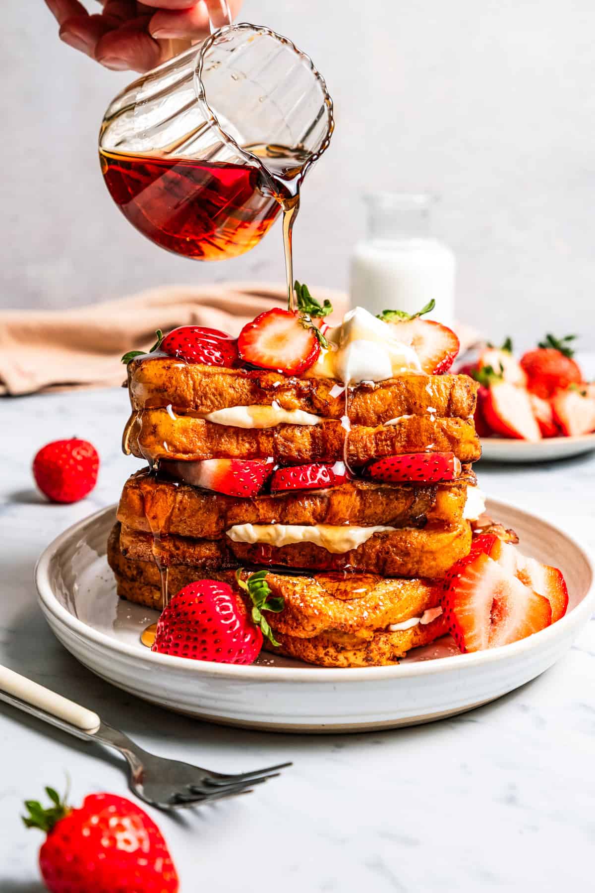 Make this cream cheese stuffed French toast with thick slices of custard-dipped brioche filled with sweet mascarpone and fresh lemon zest. Pouring maple syrup over French toast.