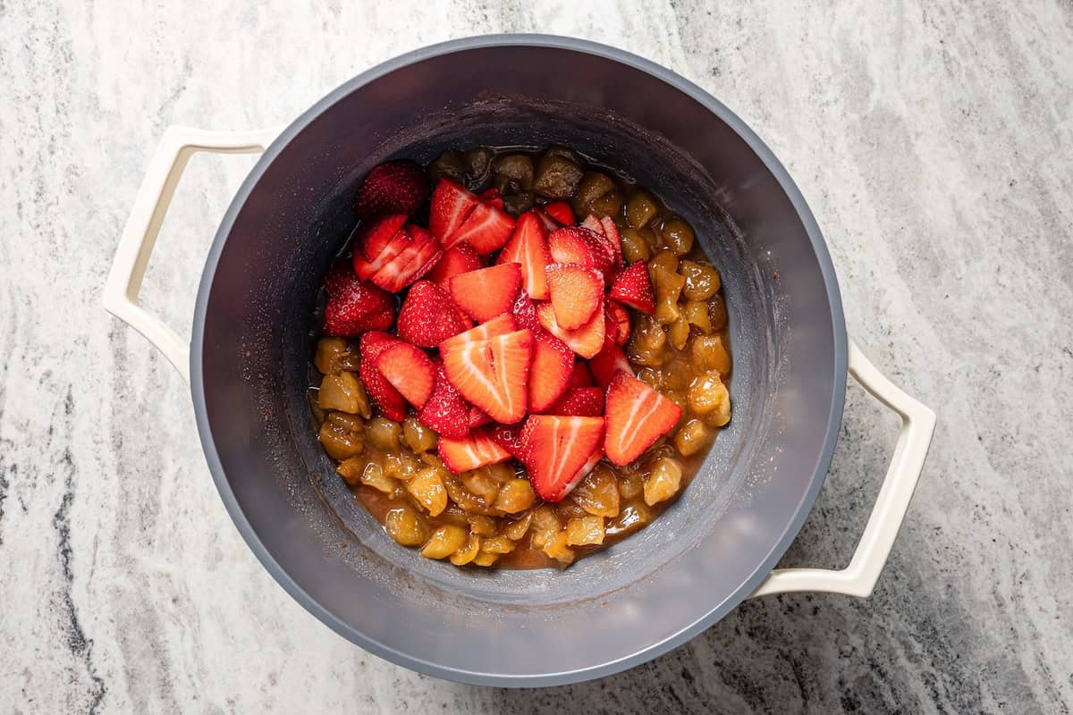 Apple berry pie is the perfect dessert to go from summer to fall! A cozy homemade apple pie bursting with fresh berries in a flaky pie crust. Strawberries added to cooked apple pie filling in a pot.