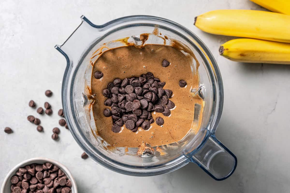Chocolate protein muffins are moist, loaded with hidden veggies, and easy to make in the blender for a high-protein breakfast or meal prep. Chocolate chips added to protein muffin batter in a blender.