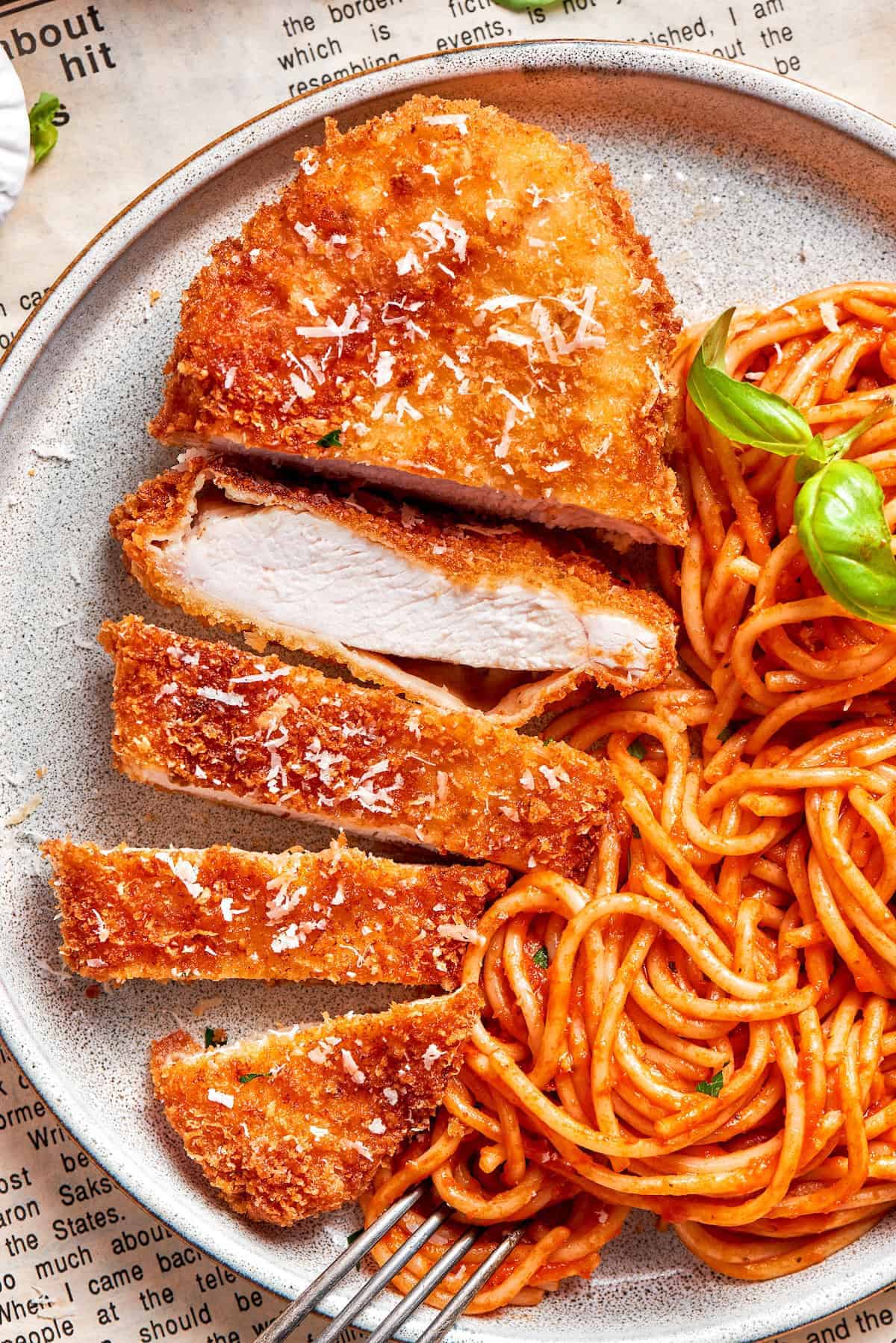 Weekly Meal Plan Breaded Romano chicken breasts sliced and arranged on a plate with a side of spaghetti.