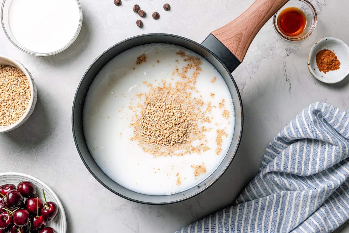 This easy overnight steel-cut oats recipe combines chewy oats, milk, vanilla, and cozy cinnamon into a delicious make-ahead breakfast. Steel cut oats added to milk in a saucepan.